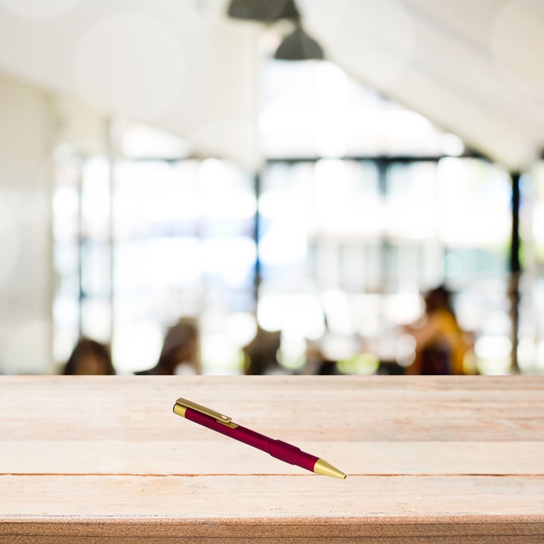 Red matte metal pen with golden parts on a wooden desk background